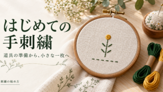刺繍枠に張った生成りの布と、緑と黄色の糸で刺した小さな植物モチーフ